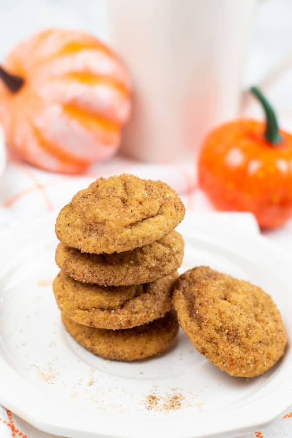 A stack of pumpkin snickerdoodles cookies on a white plate with pumpkins in the background. 