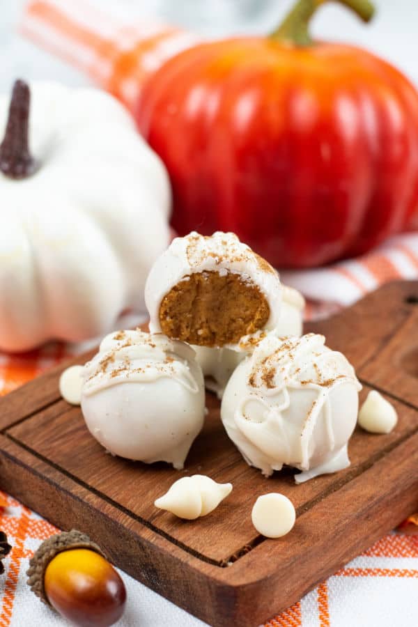 A pile of white chocolate covered pumpkin truffles, the one on top has a bite taken out of it revealing it's center. 