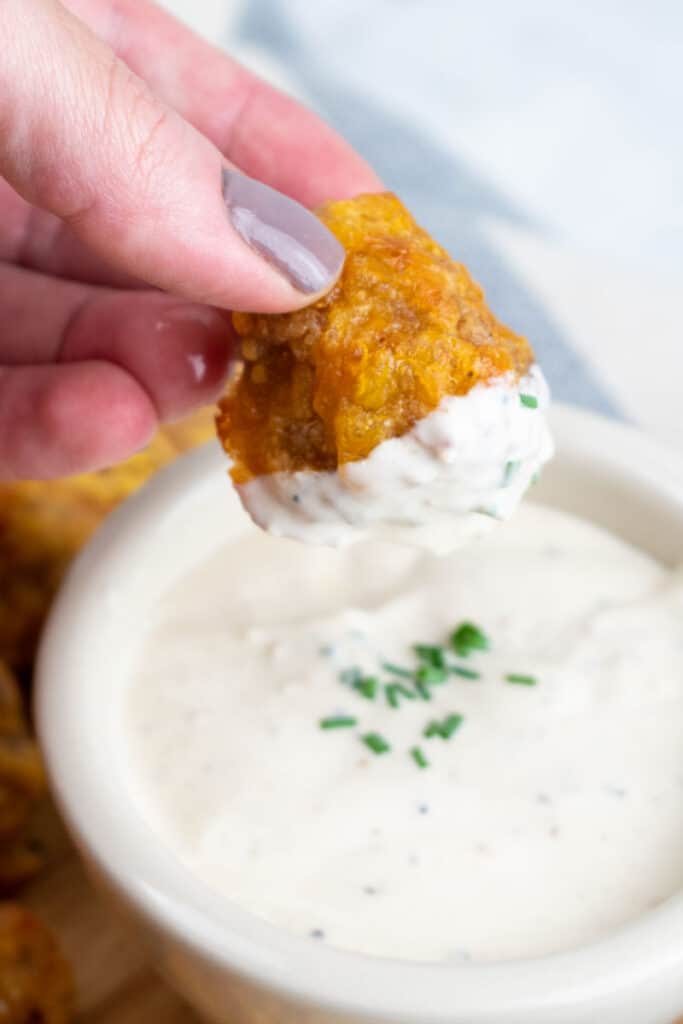 A hand dipping a sausage ball in a bowl of white dip. 