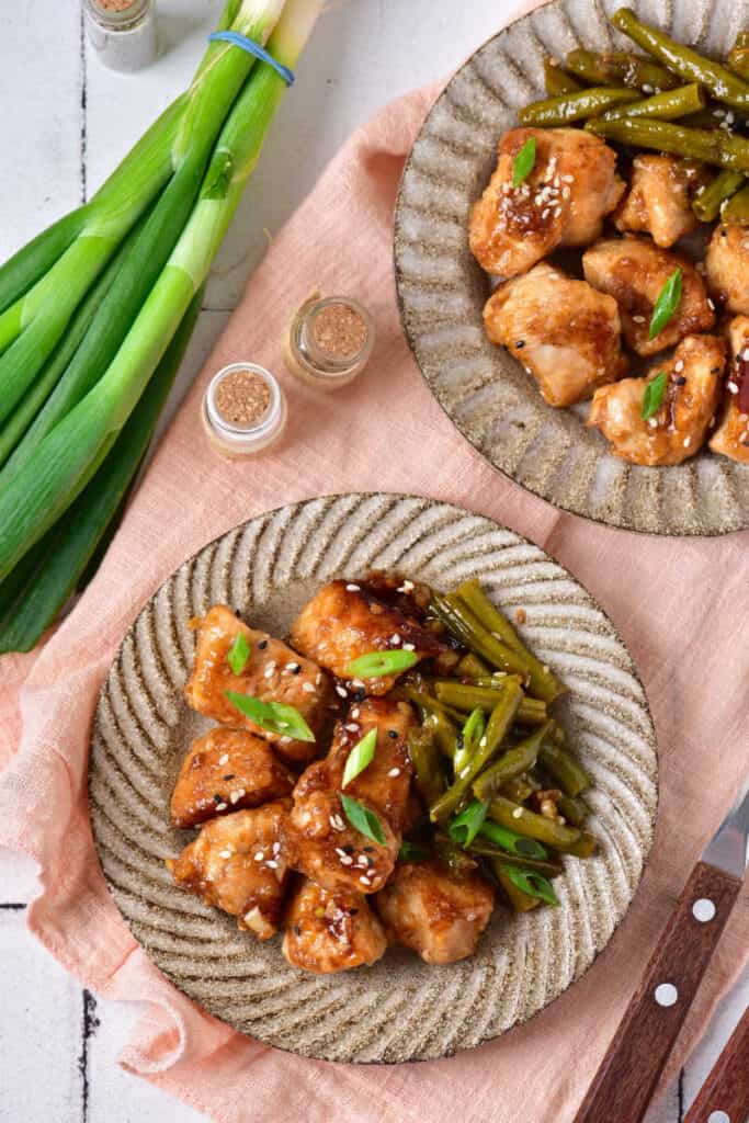an overhead shot of a table set with two plates both with sesame chicken and green beans 