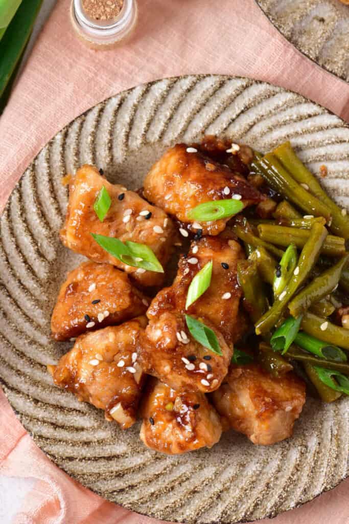 An overhead shot of a tan plate full of sesame chicken and green beans. 