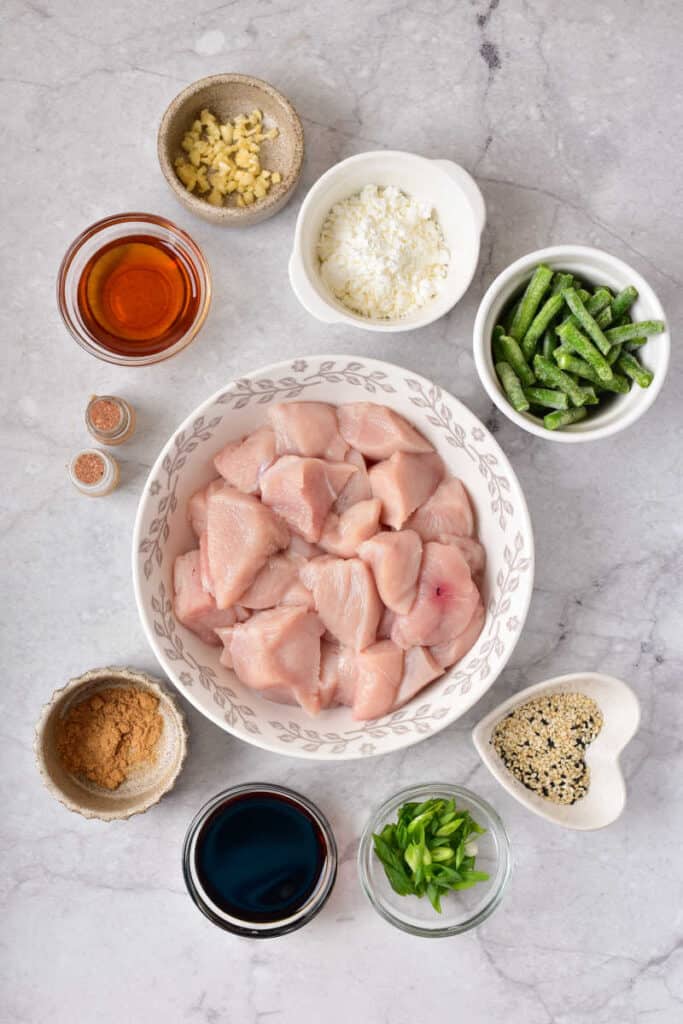 The ingredients for easy sesame chicken. Cubed chicken, salt, pepper, corn starch, soy sauce, ginger, sesame oil, green beans, green onions and sesame seeds. 