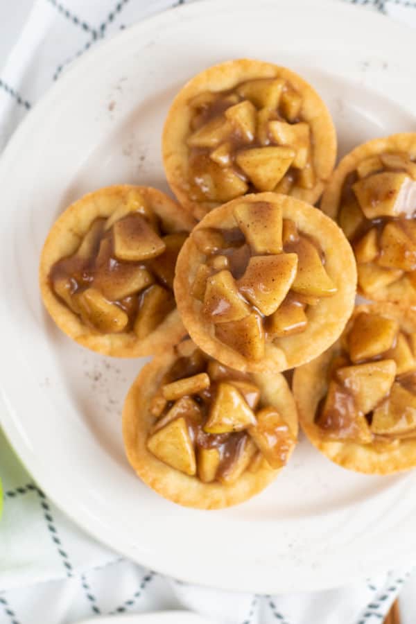 A pile of apple pie cookie cups on a white plate. 
