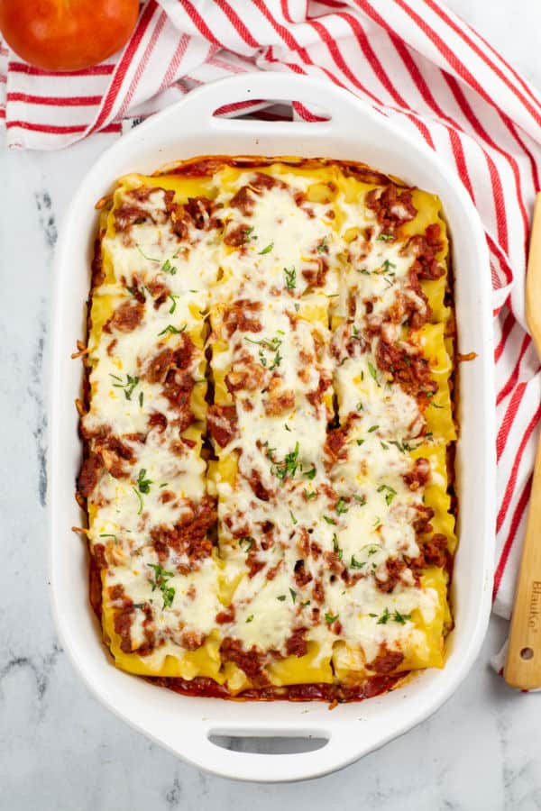 A white casserole dish filled with lasagna roll ups covered with sauce and shredded mozzarella. 