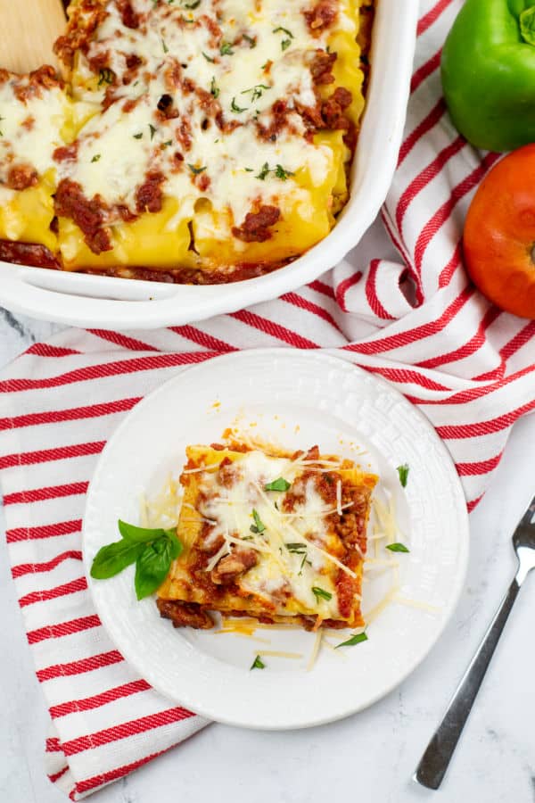 A lasagna roll up on a white plate sitting on a red and white striped linen. 