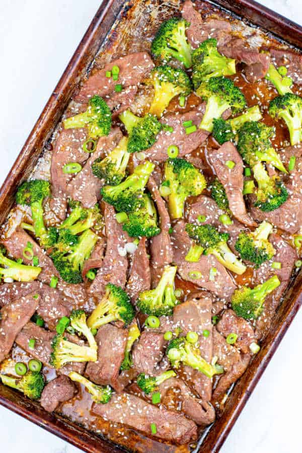 A sheet pan with beef and broccoli garnished with sesame seeds and sliced green onions. 