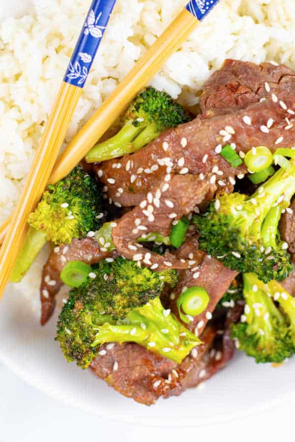 A close up of a bowl of beef and broccoli and rice with chopsticks 