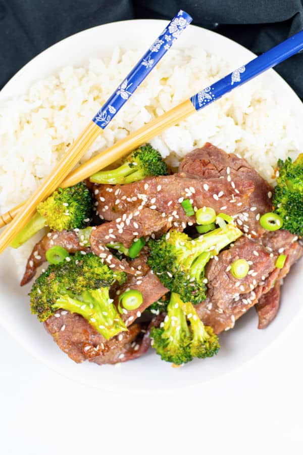 A bowl of beef and broccoli with rice and chop sticks. 