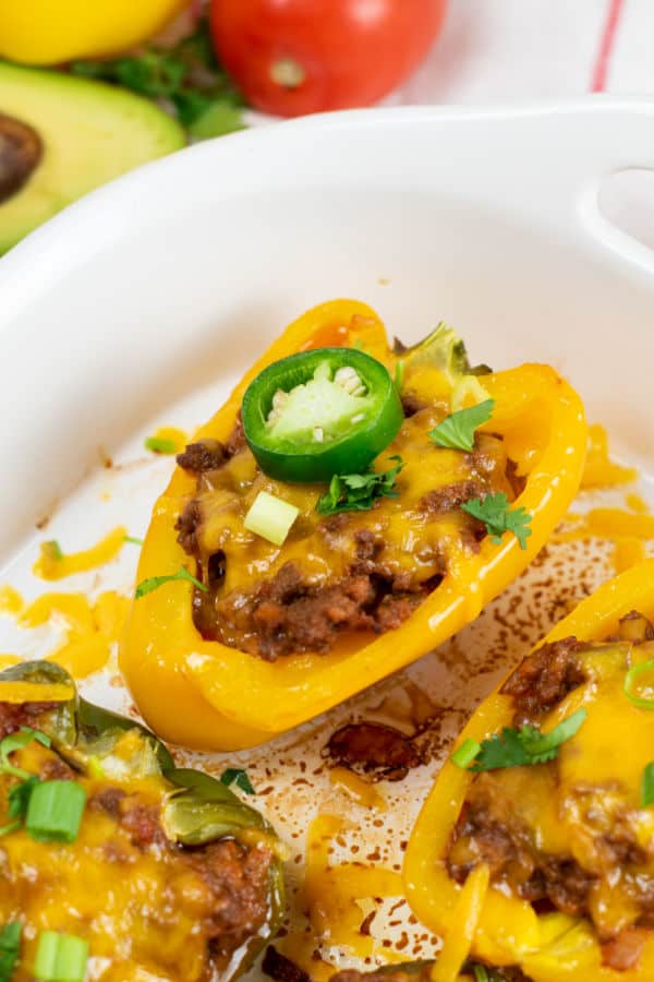 A close up of a yellow bell pepper stuffed with meat and topped with cheddar cheese and a sliced jalapeno. 