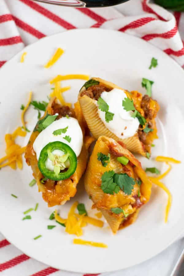 Three taco stuffed shells on a white plate. They have been garnished with sour cream, jalapeno and fresh cilantro. 