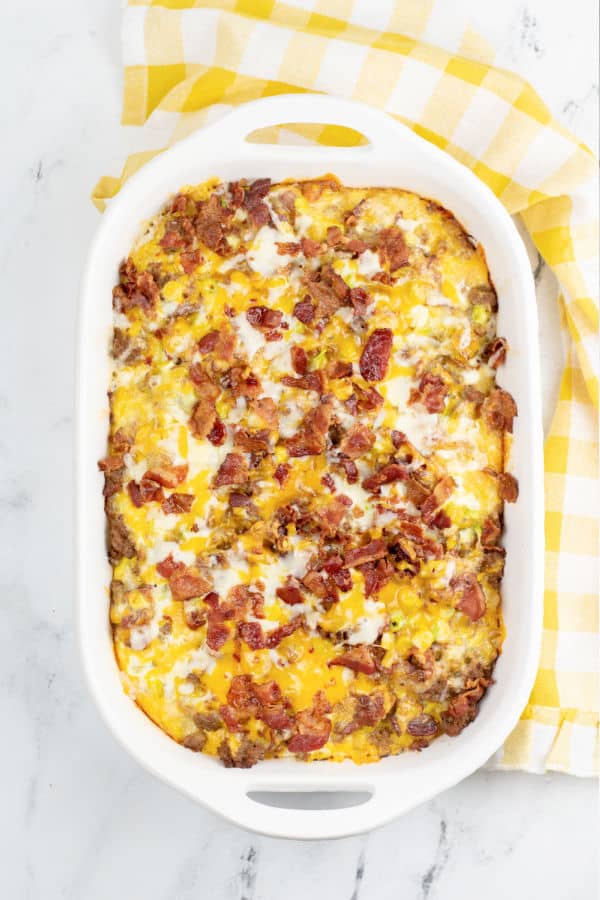 An overhead shot of a white baking pan with a tater tot breakfast casserole The top of the casserole is covered with melted cheese and bacon pieces. 