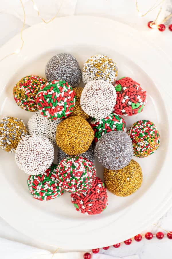 A white plate covered with a pile of Christmas brownie truffles decorated with a variety of colorful sprinkles