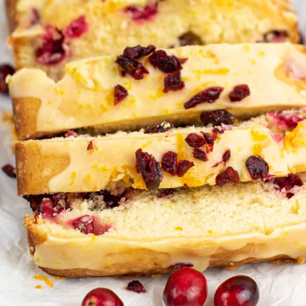 A close up of sliced cranberry orange pound cake that is drizzled with orange glaze and a chopped dried cranberries. 