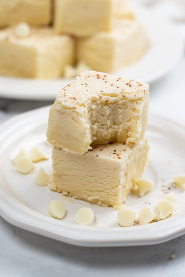 two pieces of eggnog fudge stacked on top of each other, the top piece has a bite taken out 