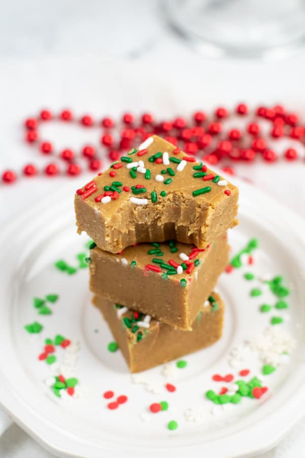 A stack of three pieces of gingerbread fudge on a white plate. The top piece has a bite taken out of it showing the soft interior of the fudge. 
