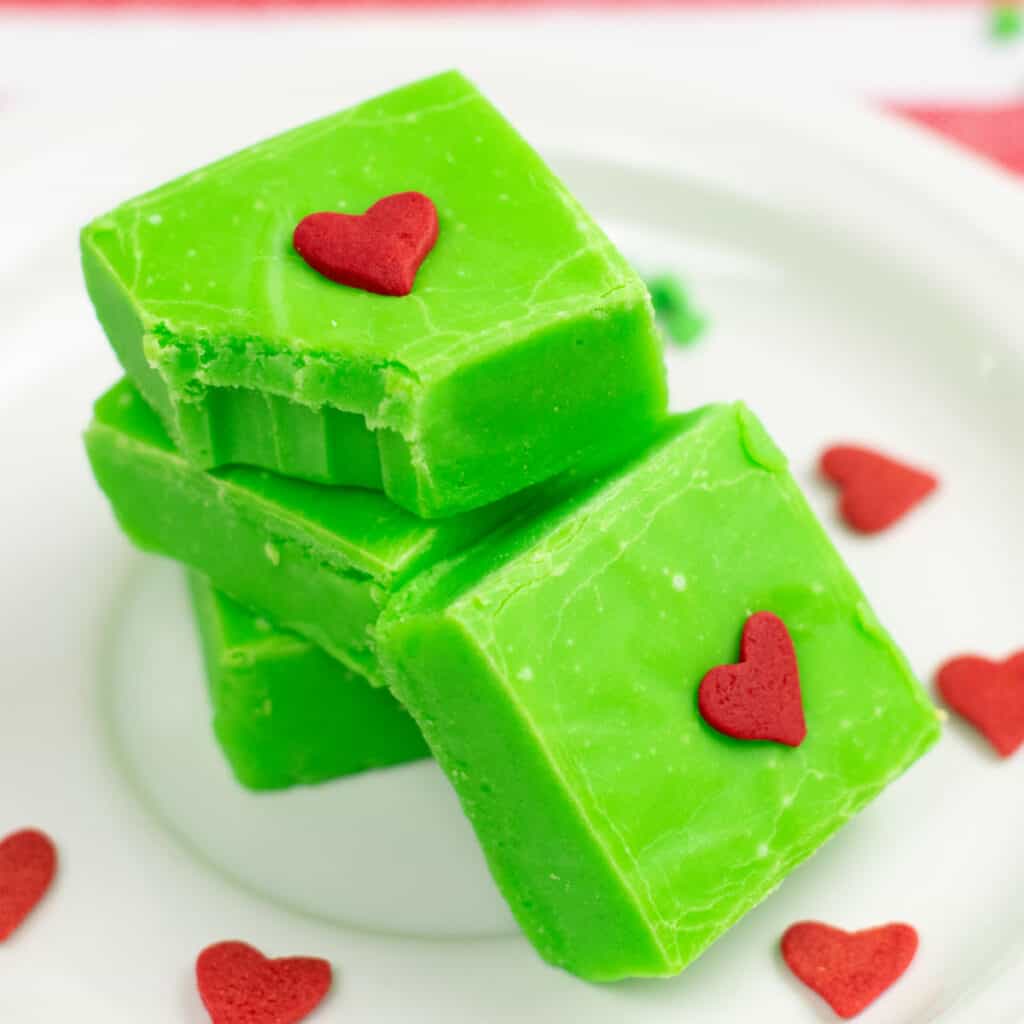 a pile of green fudge with red hearts in the center. The top piece has a bite missing showing the creamy interior of the fudge. 