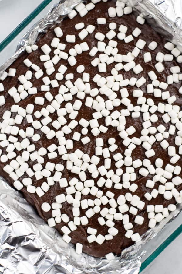 a square pan lined with foil and full of chocolate fudge sprinkled with marshmallows. 