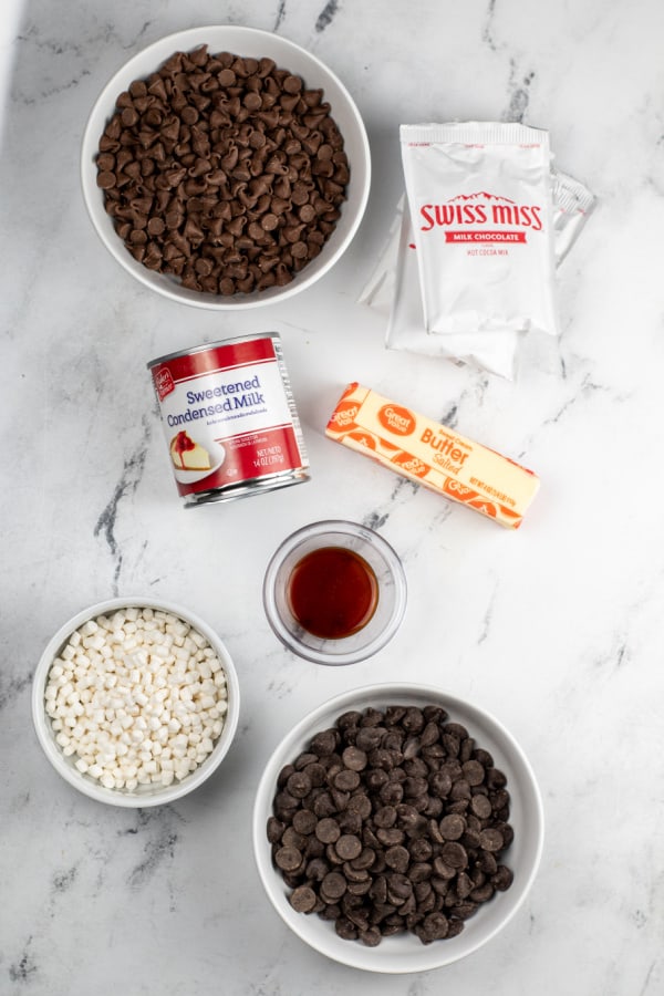 ingredients for hot cocoa fudge. Milk chocolate chips, semi sweet chocolate chips, hot cocoa mix, sweetened condensed milk, butter, vanilla and marshmallow bits. 
