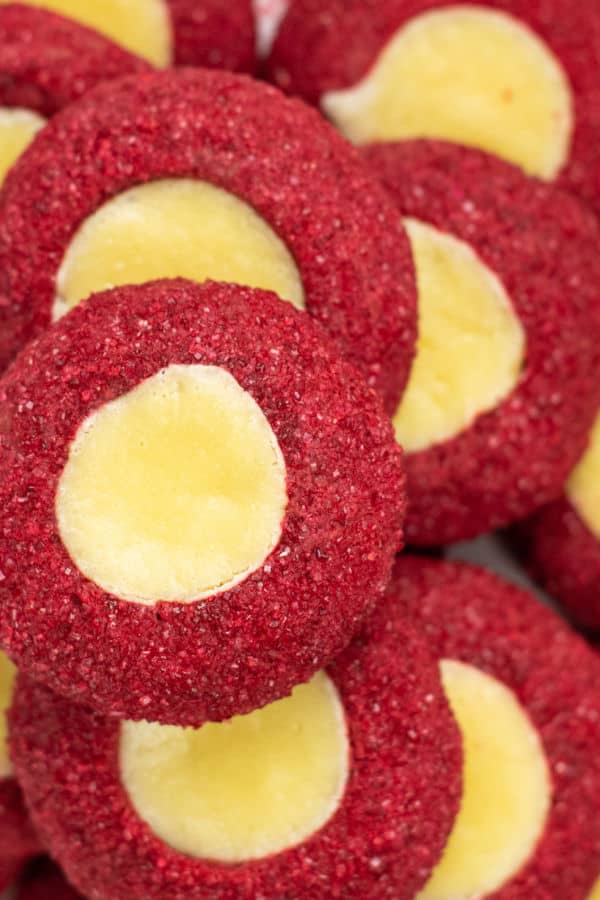 A close up of a pile of red velvet cookies. The cookies have been dipped in red sugar and are filled with a creamy cheesecake filling. 