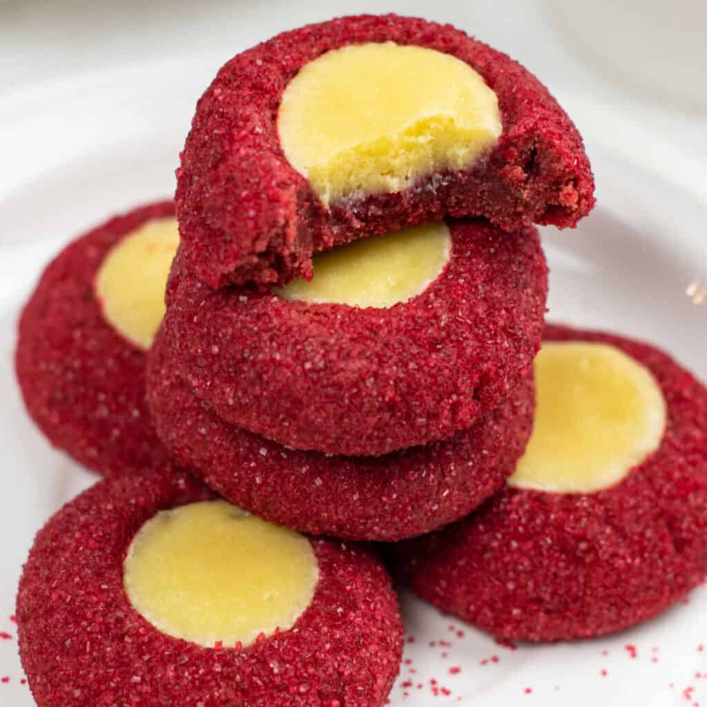 A stack of red cookies with creamy filling on a white plate. 