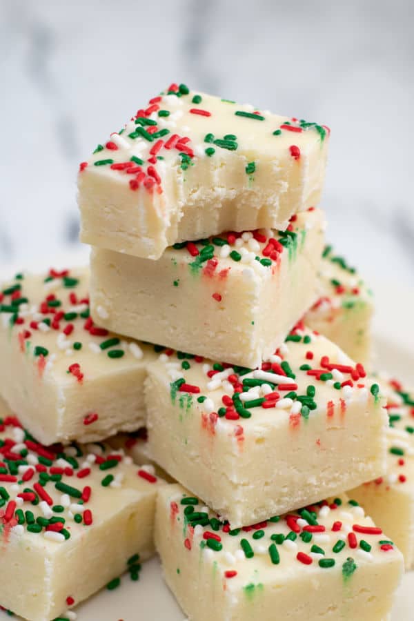 a pile of sugar cookie fudge. The top piece has a bite taken out showing the soft creamy texture of the fudge. 