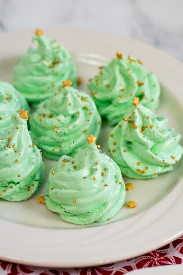 A plate filled with christmas tree shaped meringue cookies. 