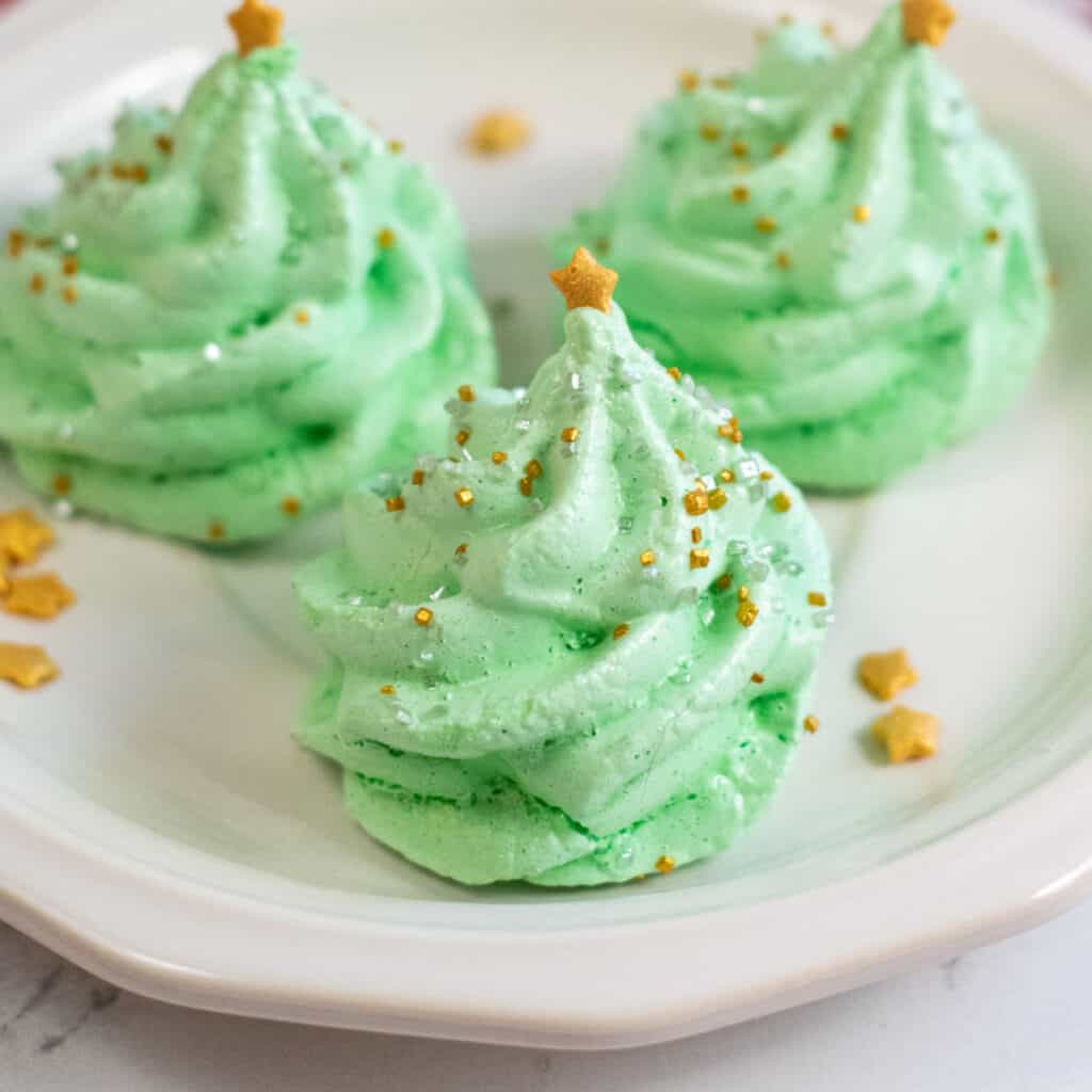A close up of a Christmas tree meringue cookie. It is green with gold and silver sprinkles and a gold star on the top. 