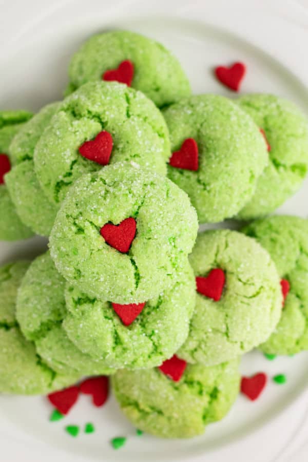A plate of green Grinch crinkle cookies. Green cookies with red heart sprinkles pressed into the center. 