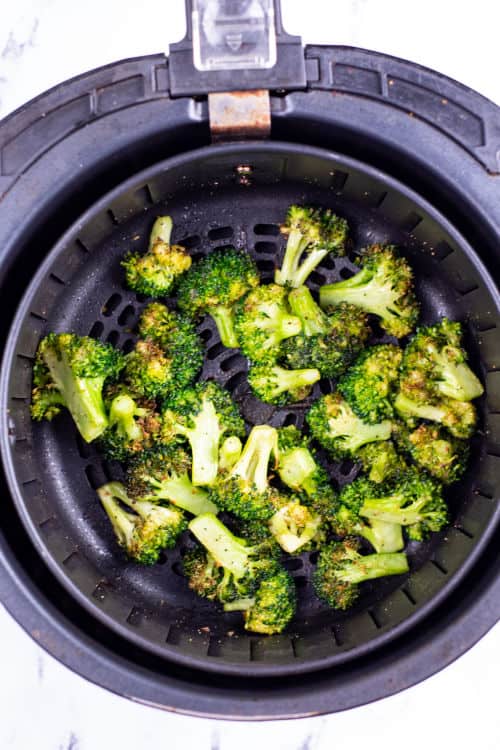 An overhead view of a pile of cooked broccoli in the basket of an air fryer.