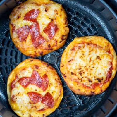 Three air fryer mini pizzas in the basket of an air fryer two are topped with pepperoni and one is topped with cheese