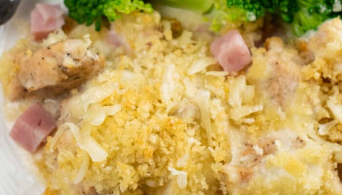 A close-up of chicken cordon bleu casserole with broccoli on a white plate.