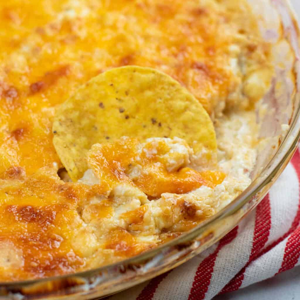 A close up of cheesy Maryland crab dip with a round corn tortilla chip dipped in it. 