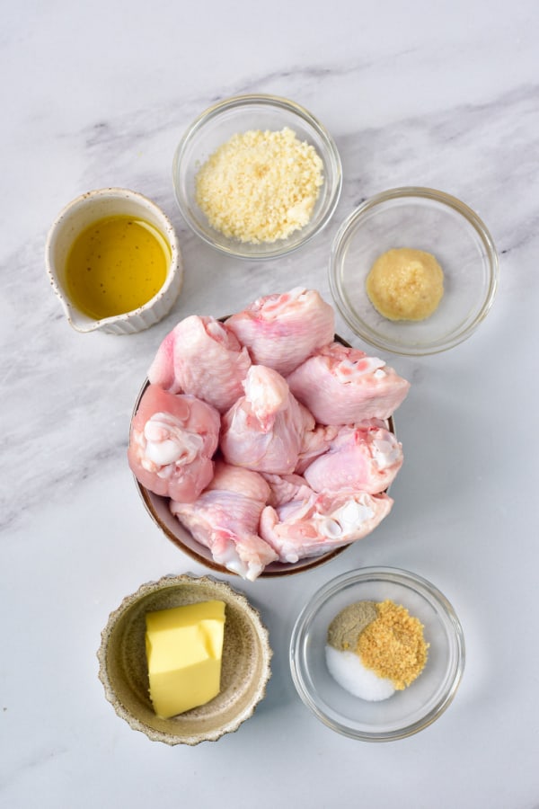The ingredients for garlic parmesan wings. Fresh chicken wings, olive oil. parmesan cheese, butter, salt, minced garlic, pepper and onion powder on a marble counter top. 