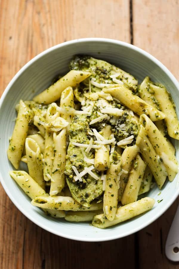 A bowl with penne pasta coated with pesto and sprinkled with cheese. 