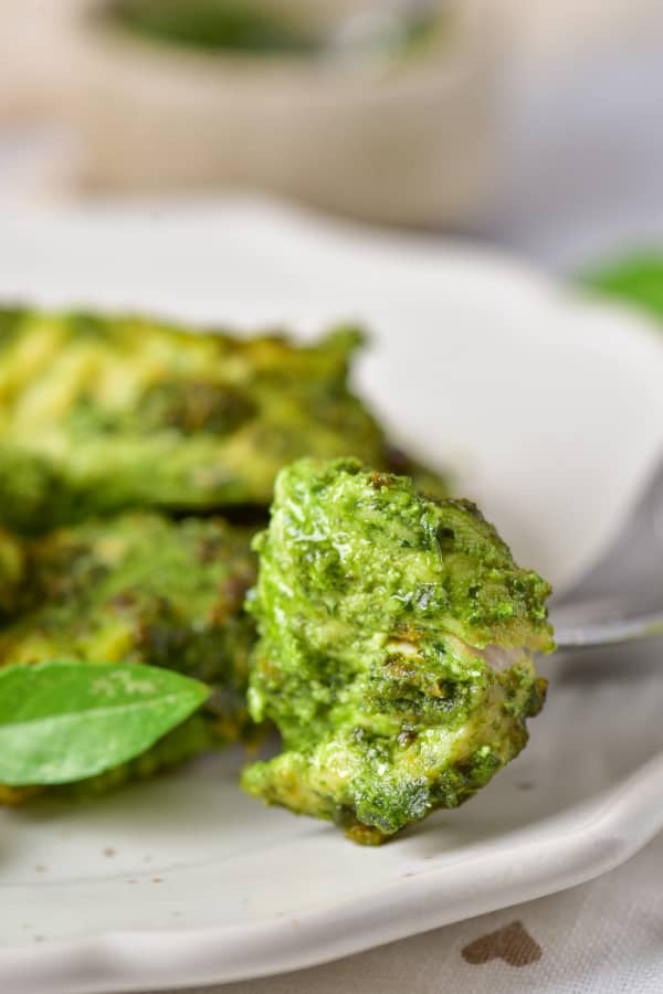 A close up of a piece of chicken coated with pesto sauce. 