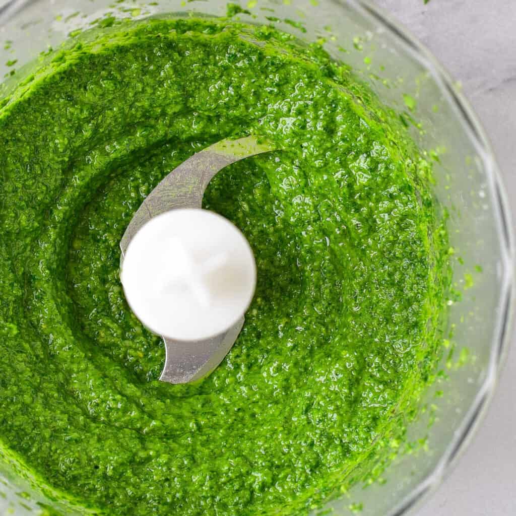 A food process with bright green pesto in it. 