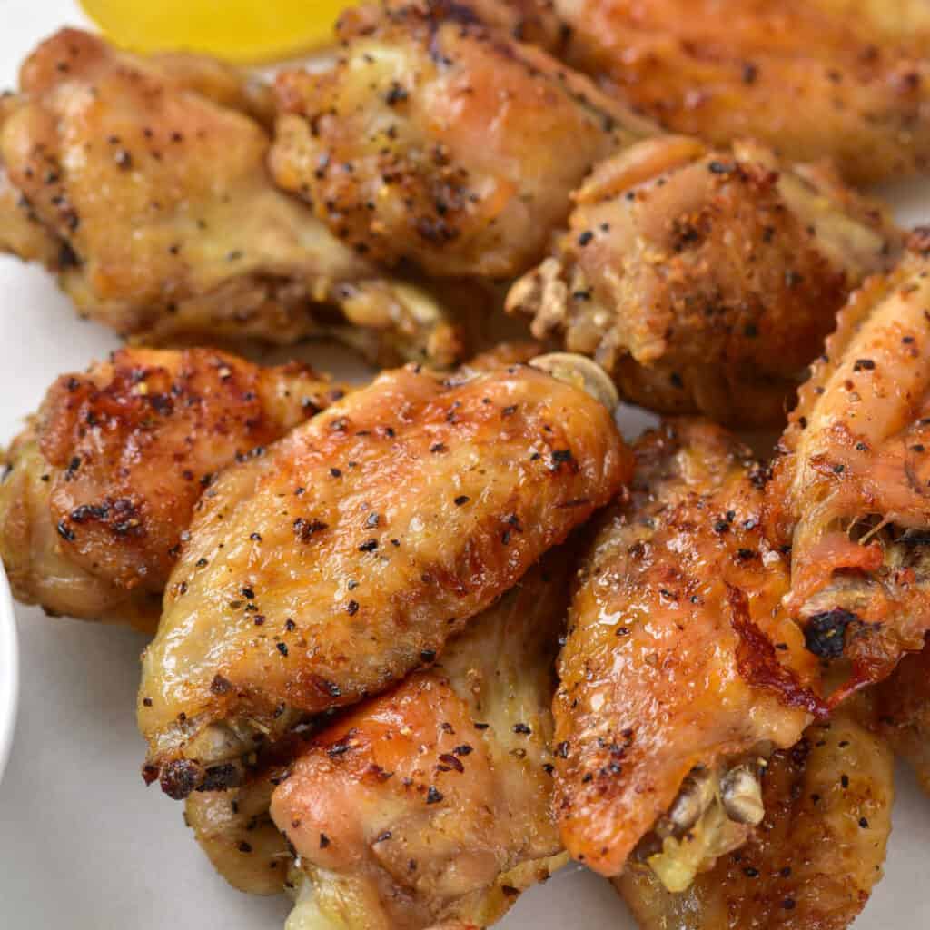 A close up of golden brown chicken wings with lemon pepper on them 