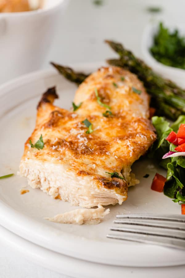 A white plate with a piece of mayo parmesan chicken, salad and asparagus. 