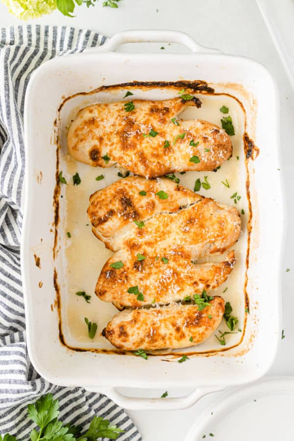 A white baking dish with four golden brown chicken breasts in it. 