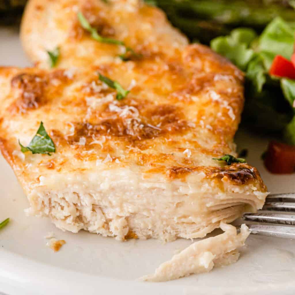 A piece of parmesan crusted chicken with a bite taken out showing the moist chicken breast. 