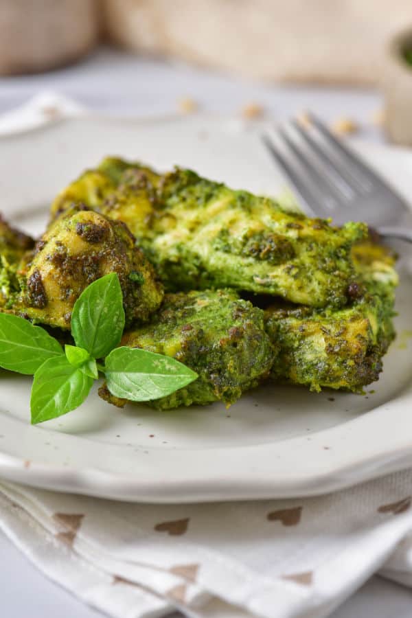 A side view of a pile of pesto chicken on a white plate with a fork in the background. 