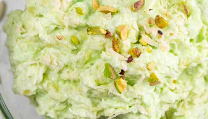A close-up of a large glass bowl of pistachio pudding salad topped with crushed pistachios.