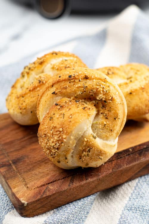 Several air fryer garlic knots on top of a wooden cutting board on a dish towel.