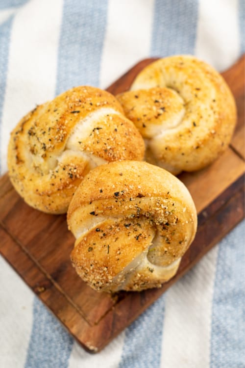 Several air fryer garlic knots on top of a wooden cutting board on a dish towel.