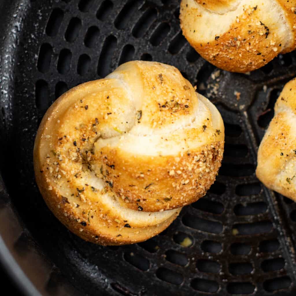An overhead view of a batch of garlic knots in the basket of an air fryer.