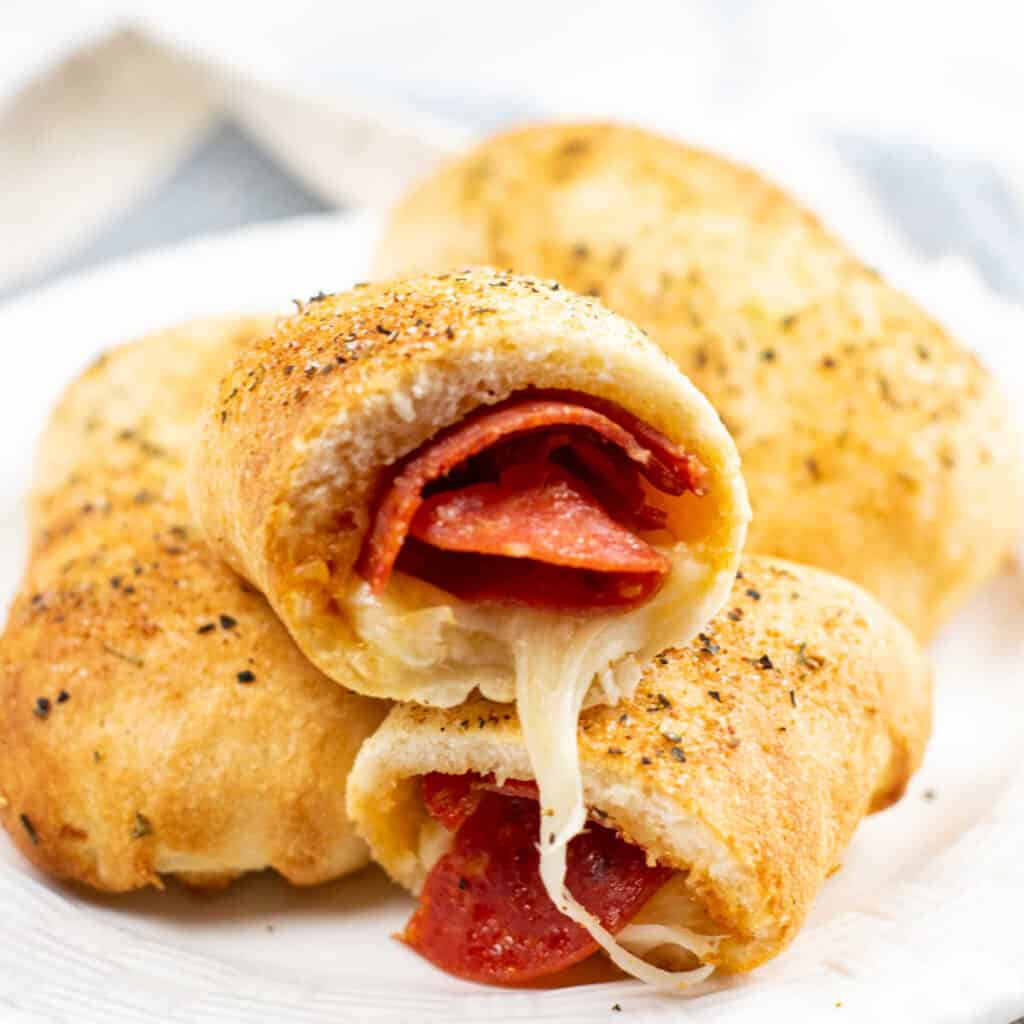A small white plate of air fryer pepperoni rolls sitting on a dish towel.