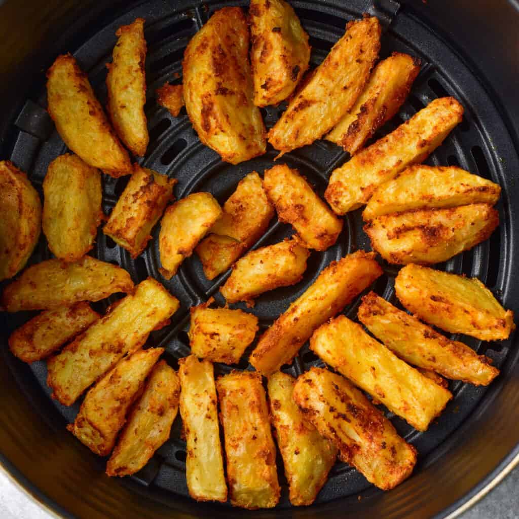 An overhead view of a batch of air fryer potato wedges in the basket of an air fryer.