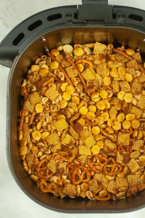 An overhead view of a batch of chex mix sitting in the basket of an air fryer.
