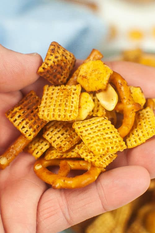 A close-up of a hand holding a handful of air fryer chex mix.