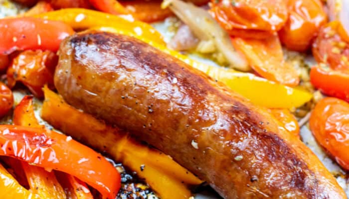 A close-up of a sheet pan of Italian sausage and various mixed vegetables.
